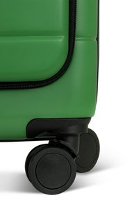 Grüner Hartschalenkoffer mit schwarzem Reißverschluss, der eine strukturierte Oberfläche und zwei schwarze Rollen für die Mobilität aufweist.