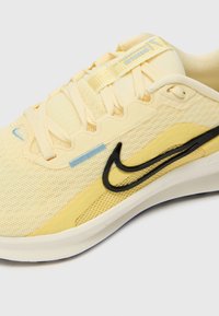 Rumene športne čevlje, ki so narejeni iz mrežaste in sintetične materialov, značilen črni Swoosh akcent, teksturirane površine in kontrastni svetlo modri detajli.