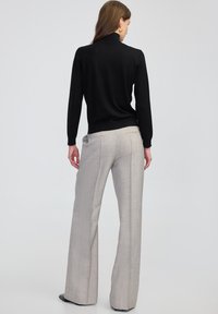 Maglione nero a collo alto con maniche lunghe abbinato a pantaloni grigi chiari a gamba larga con un sottile motivo a righe e pieghe frontali.