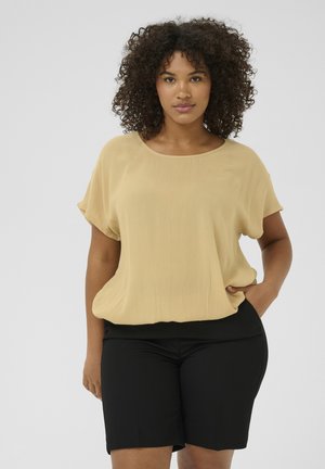 Blusa corta amarilla claro de manga corta con un corte relajado y escote redondo; combinada con pantalones cortos negros ajustados. Textura suave, diseño minimalista.