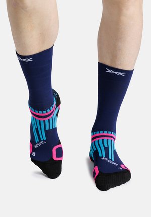 Benen met marineblauwe, zwarte, roze en turquoise sportkousen met gestreepte patronen, gezien van achteren en van de zijkant tegen een witte achtergrond.