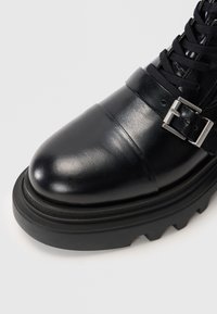 Black leather ankle boot with a rounded toe, buckle detail, and a textured rubber sole featuring distinct tread patterns.