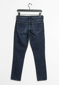 Jean en denim bleu foncé suspendu à un cintre noir, vu de dos avec les poches et les passants de ceinture visibles.