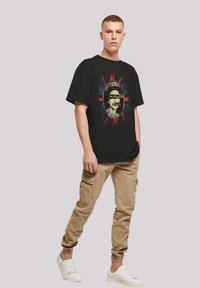 Black t-shirt featuring a graphic print with a circular design and text, set against a multicolored background. Worn with beige cargo pants.