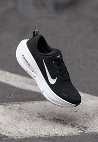Juodas sportinis batelis su tinklo viršutine dalimi, baltu Nike swoosh logotipu ir minkštu baltu vidurio padu. Pasižymi tekstūruotu dizainu ir raišteliais.