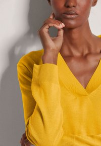 Gelbes V-Ausschnitt-Sweatshirt mit gerippten Bündchen und Ausschnitt, hergestellt aus einem weichen Strickmaterial; figurbetontes Design, das sich sanft am Körper anpasst.