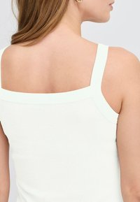 Bílý žebrovaný top bez rukávů s širokými ramínky a čtveratým výstřihem. Hladká textura, minimalistický design, vhodný na vrstvení.