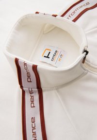 Sudadera blanca de cuello alto con media cremallera, acentuada con detalles de marca en rojo y marrón a lo largo de los hombros.