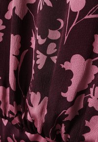 Tela púrpura oscura con superficie texturizada que presenta grandes y audaces patrones florales rosa y detalle fruncido en la parte inferior.