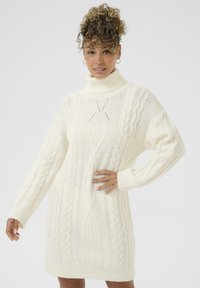 Abito in maglia bianco con collo alto, caratterizzato da motivi a treccia e maniche lunghe, tessuto testurizzato e vestibilità comoda.