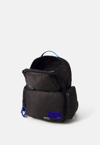 Black nylon backpack with multiple zippered compartments, a blue handle, and a blue logo patch on the front. Smooth, matte texture.