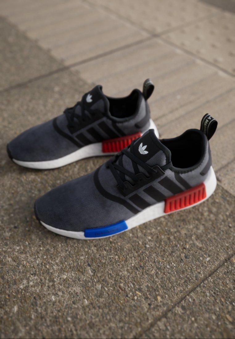 Schwarze und graue Sportschuhe mit Obermaterial aus Wildleder, schwarzen Streifen und auffälligen Akzenten in Rot und Blau. Weiße Gummisohle.