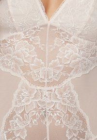 Béžový body s jemnými kvetinovými čipkovými detailmi, hlbokým výstrihom do V a hladkou, priesvitnou textúrou, ktorá zdôrazňuje rôzne kvetinové vzory.