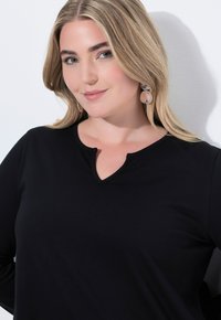 Černý dlouhý rukáv top s detaily výstřihu ve tvaru klíčové dírky, hladká textura a přiléhavý silueta. Součástí jsou visící náušnice.