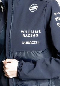 Granatowa kurtka z połączeniem gładkiego i teksturowanego materiału, z białymi logo Gulf, Williams Racing i Duracell na klatce piersiowej.