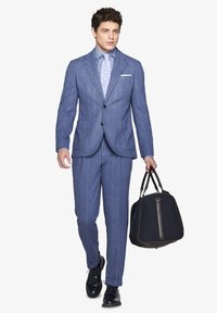 Completo a righe blu chiaro con giacca aderente e pantaloni coordinati, abbinato a una cravatta decorata e che porta una borsa a tracolla scura.