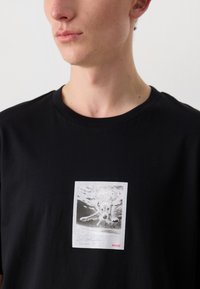Maglietta nera in cotone con una stampa grafica rettangolare di un cane che nuota nell'acqua, con il testo "Los Angeles Summer '25" e il logo rosso "HUGO".