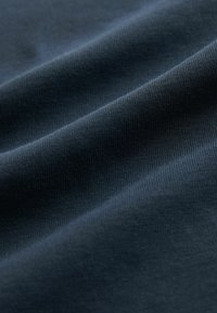 Tamnoplava tkanina glatke teksture s diskretnim rebrastim uzorkom. Materijal izgleda mekan i nježno se nabori u nabore.