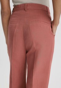 Roze stoffen broeken met een zachte textuur, met een getailleerde pasvorm, riemlussen en twee achterzakken.