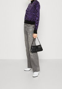 Sac à main en cuir noir avec bandoulière en chaîne, pull imprimé tigre violet, jean gris déchiré avec éclaboussures de peinture blanche et bottines blanches.