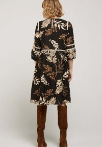 Robe noire avec un motif floral beige et rouille, présentant des manches trois-quarts et une taille cintrée. Bottes en suède à hauteur de genou.