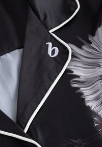 Fekete szatén anyag fehér szegéllyel és virágmintával. A galléron hímzett logó található a részletekért. Simák, selymes tapintású.