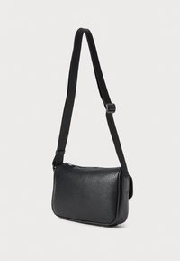 Melna teksturēta ādas crossbody soma ar regulējamu melnu auduma siksnu un aizdari augšpusē, parādīta uz vienkārša gaiša fona.