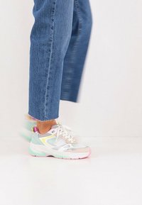 Πολύχρωμο αθλητικό παπούτσι με επάνω μέρος από δίχτυ, ανοιχτό γκρι, παστέλ πράσινο, ροζ λεπτομέρειες και λευκά κορδόνια. Φορεμένο με μπλε κοντά τζιν.