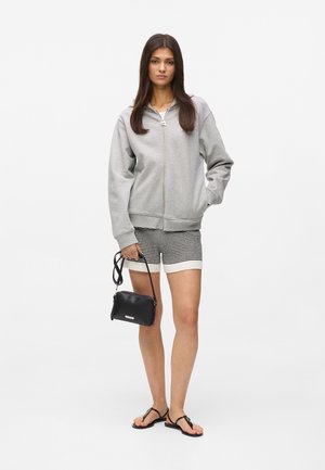 Sweat à capuche gris zippé, short rayé, sac à main noir et tongs. Présente une coupe décontractée, une texture douce et un design simple.