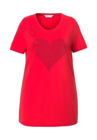 Rød T-shirt med korte ærmer, der har et stort sort nitterhjerte designet i midten og et lille sort bogstav "Q" på venstre skulder.