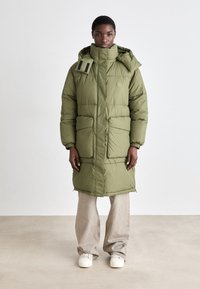Olive green padded long coat with a high collar, adjustable drawstring hood, and two front pockets. Smooth texture, minimalistic design.