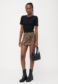 Fekete bordás, rövid ujjú felső, leopárdmintás mini szoknya, fekete bokacsizma és egy kis fekete kézitáska studokkal díszítve.