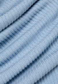 Hellblauer Strickstoff mit einem strukturierten Rippenmuster. Das Garn wirkt weich und weist leichte Farbnuancen auf, die Tiefe verleihen.