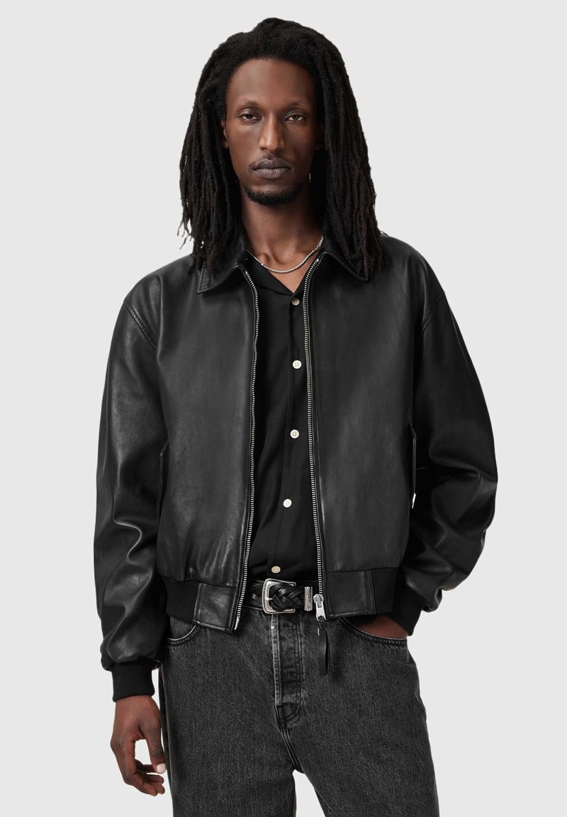 Czarna skórzana kurtka typu bomber z zamkiem z przodu, ściągaczami na rękawach i u dołu. Noszona na czarnej koszuli zapinanej na guziki z jasnymi guzikami.