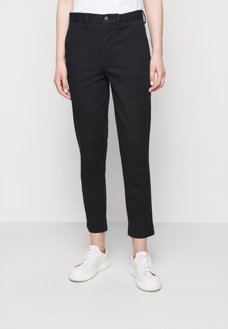 Svarta slim-fit chinos med fram- och bakfickor, avslutade med en klämsknapp. Bärs med vita sneakers.