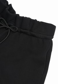 Pantalon de survêtement noir avec taille élastique, cordon de serrage noué en un nœud et poche latérale visible sur fond blanc.