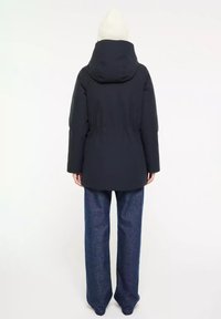 Navyblauwe pufferjack met capuchon, voorzien van een getailleerde taille en een gladde textuur, gedragen over brede denim broek.