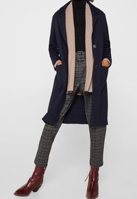 Granatowy długi płaszcz na kremowym kardiganie, zestawiony z kratkowymi spodniami i bordowymi botkami za kostkę. Posiada szerokie klapy i boczne kieszenie.
