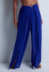 Pantalons larges en voile bleu avec une grande fente de chaque côté et un accent doré à la taille. Tissu léger pour une allure fluide.