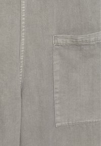 Gros plan sur un tissu gris avec une poche rectangulaire cousue et une couture verticale sur le côté gauche.