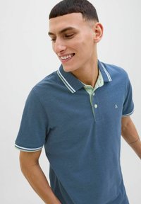 Blauwe polo met een lichtgroene kraag, voorzien van witte strepen op de kraag en mouwranden, gemaakt van gestructureerde stof met een logodetail.