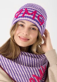 Gestreifte Strickmütze in Lila und Pink mit "OMG" in Rot, kombiniert mit einem passenden gestreiften Schal. Weiche Textur, warmes Design.
