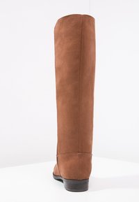 Botte mi-montante en suédine marron avec tige ajustée, bout arrondi et petit talon. Texture lisse avec des détails de coutures discrètes le long de la couture.