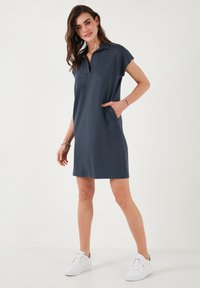 Navy blue polo-style dress with short sleeves, pocket on the side, and a relaxed fit, paired with white sneakers on a plain background.