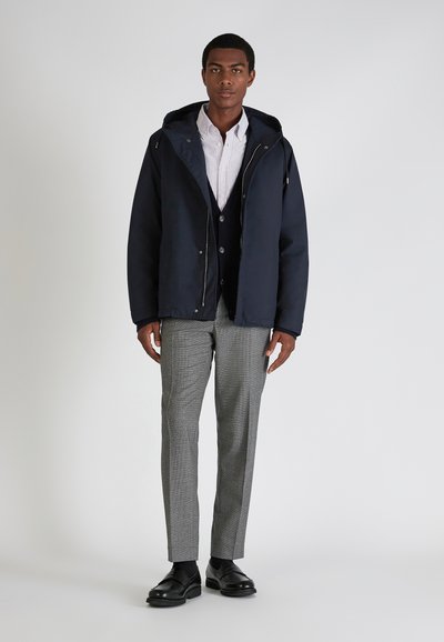 Navy hooded jacket with a zip closure, paired with a buttoned white and navy striped shirt, gray checkered trousers, and black shoes.