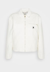 Vit denimjacka med krage, guldfärgad dragkedja och en vänster bröstficka med logotyp. Mjuk textur och avslappnad silhuett.