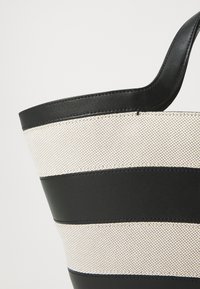Czarna i kremowa torba tote w paski, wykonana z teksturowanej tkaniny i gładkich skórzanych akcentów, z zaokrąglonym dnem i solidnymi uchwytami.