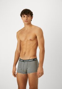 Csíkos bokszernadrág söt�étkék és fehér színben, fekete derékpánttal, amelyen a "JACK & JONES" márkaneve található. Simogató anyag, testhezálló fazon.