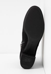 Semelle de botte noire avec adhérence texturée, talon étiqueté "ANT SLIDE", fermeture éclair visible sur le côté, sur fond blanc.