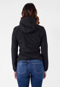 Giacca nera leggera con cappuccio, caratterizzata da una texture liscia e una silhouette aderente, abbinata a jeans di denim blu con dettagli di cucitura discreti.